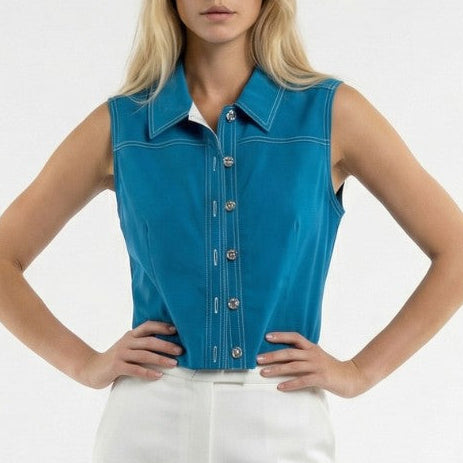 Woman wearing a blue sleeveless denim shirt and white pants on a white background