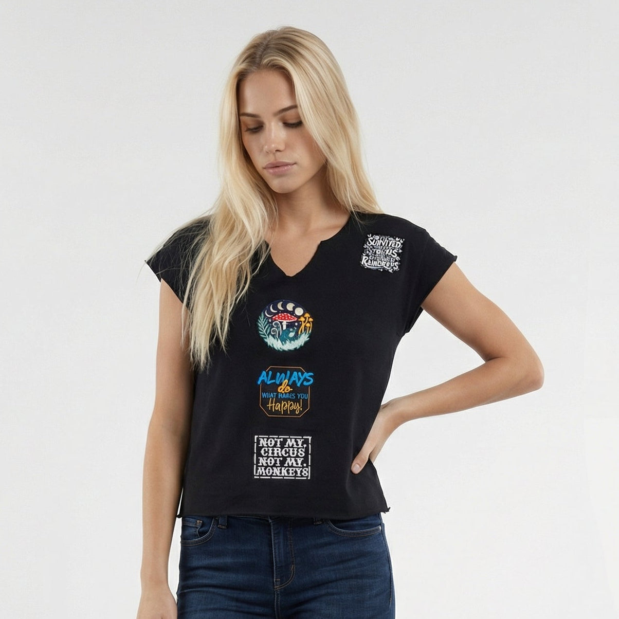 Woman wearing a black t-shirt with graphics and text, dark jeans, and black boots on a white background